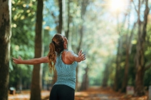 Frau streckt während einer Joggingrunde im Wald die Arme aus