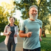 Fröhliches Ehepaar, das gemeinsam an Wettkämpfen teilnimmt und an der frischen Luft joggt. Aktive Menschen in Sportkleidung beim Cardio-Training.