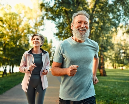 Fröhliches Ehepaar, das gemeinsam an Wettkämpfen teilnimmt und an der frischen Luft joggt. Aktive Menschen in Sportkleidung beim Cardio-Training.