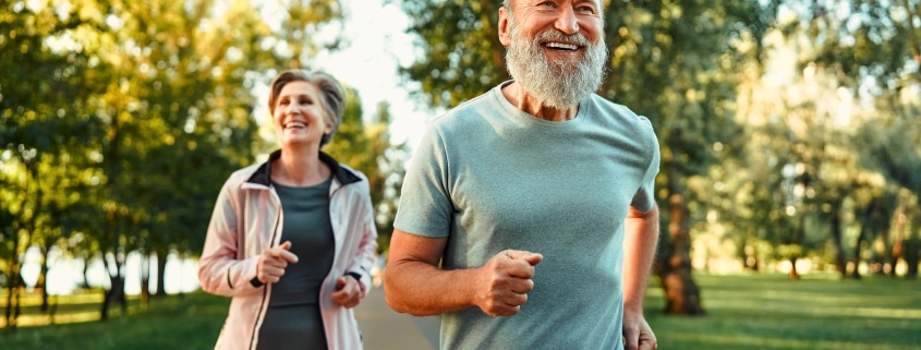 Fröhliches Ehepaar, das gemeinsam an Wettkämpfen teilnimmt und an der frischen Luft joggt. Aktive Menschen in Sportkleidung beim Cardio-Training.