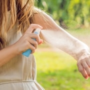 Frau sprüht Insektenschutzmittel auf Haut im Freien