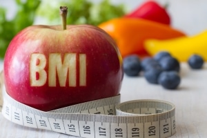 Roter Apfel mit Text BMI und Maßband vor Hintergrund von Obst und Gemüse, Diät und gesundes Gewicht Konzept